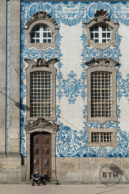 Aaron sitting in front of the azulejos on the wall of the Igreja do Carmo church in Porto, Portugal